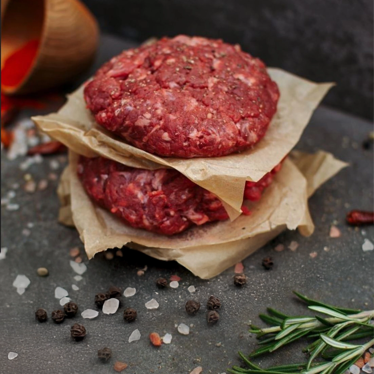 Zwei Burger Patties übereinander getürmt mit Fleischpapier getrennt, als Deko liegen Salz- und Pfefferkörner.