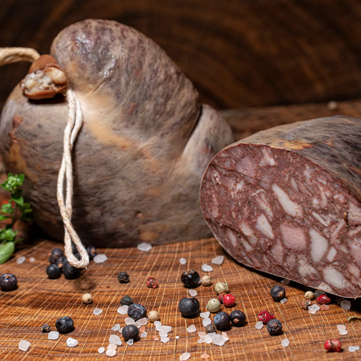 Hausmacher Blutwurst ungeräuchert, angeschnitten auf einem Holzbrett mit Salz- und Pfefferkörnern als Deko.