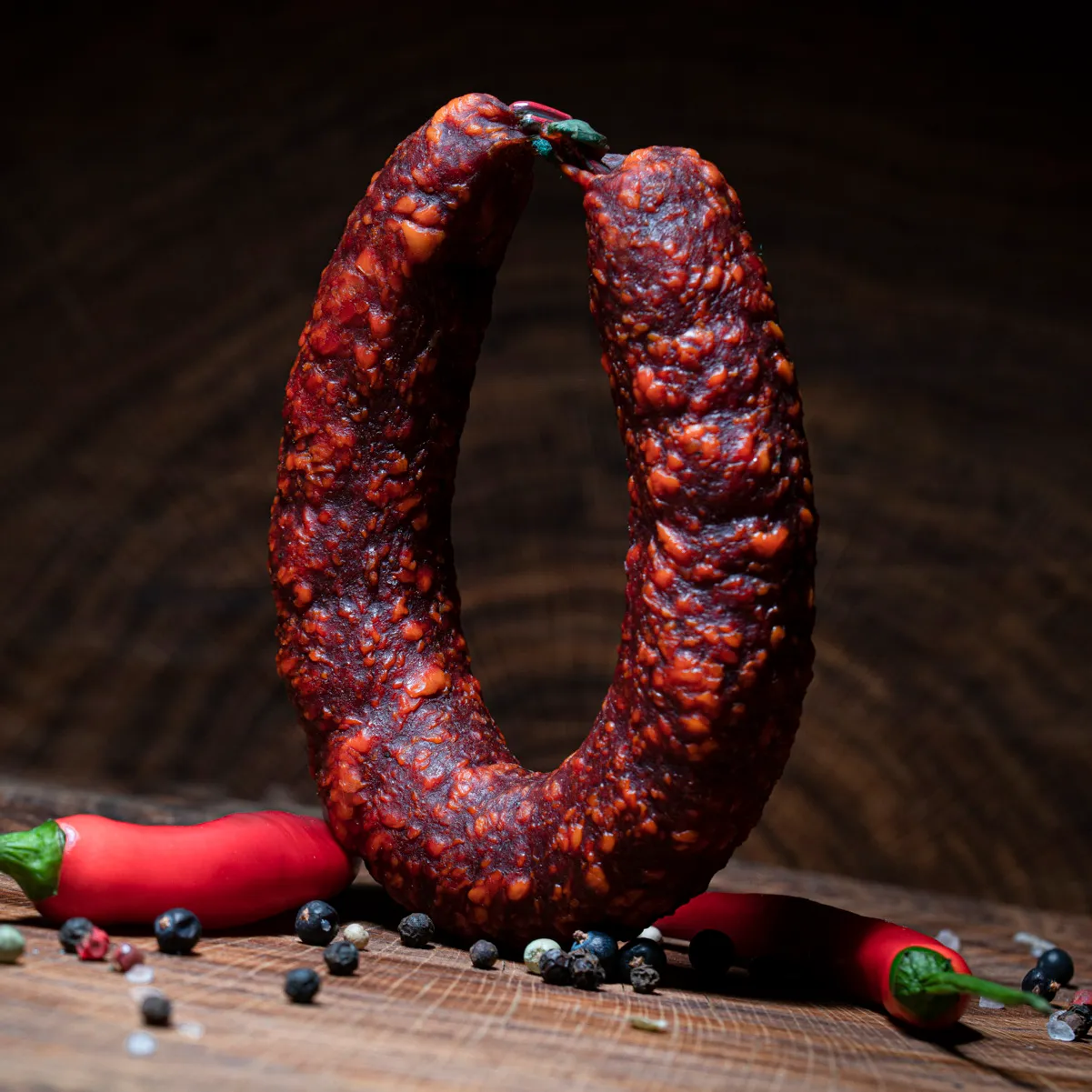 Unsere extra scharfe Höllenwurst als Delikatesse! Extra scharfe Höllenwurst mit Deko-Chili auf Tischplatte.