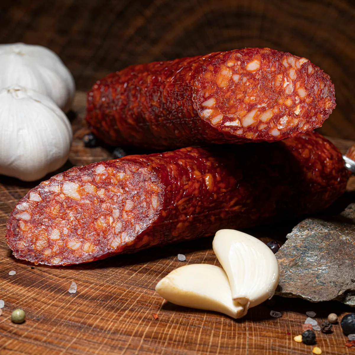Entdecke unsere Kolbaszsalami voller Genuss! Kolbaszsalami aufgeschnitten auf Tischplatte dazu Knoblauchzehen als Deko.