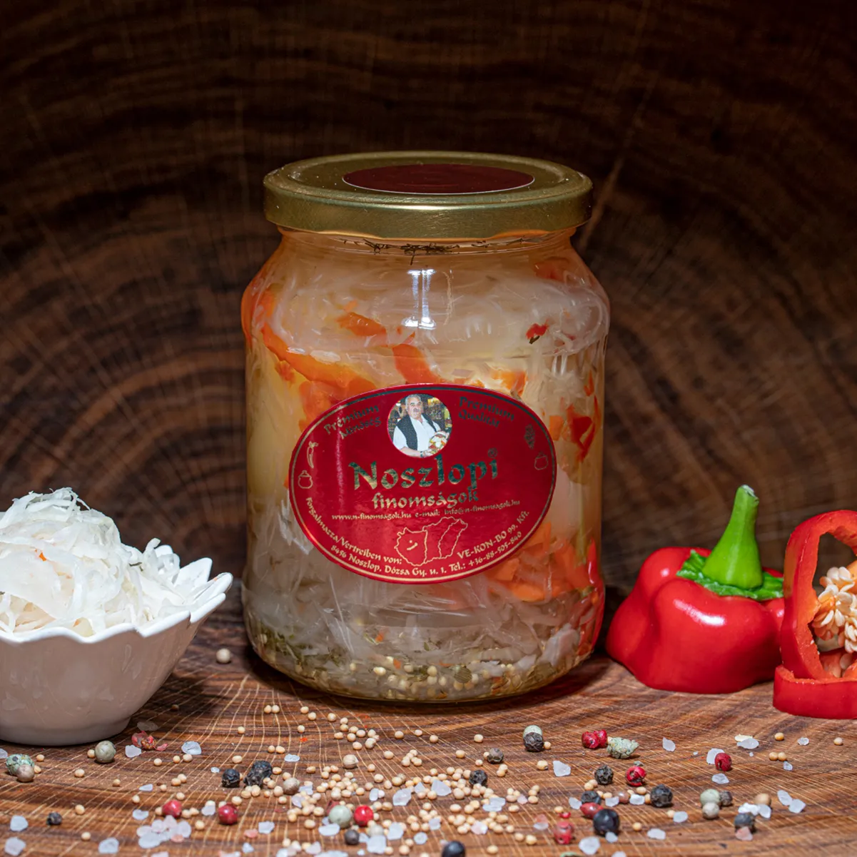 Noszlopi ungarisches, scharfes Apfelpaprika mit Kraut im Glas jetzt bestellen. Noszlopi ungarisches, scharfes Apfelpaprika mit Kraut im Glas auf Holzbrett.