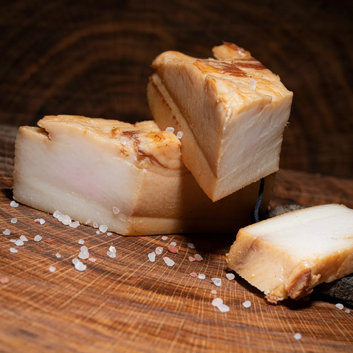 Geräucherter Mangalitza Wollschwein Speck jetzt bestellen. Geräucherter Mangalitza Wollschwein Speck mit Salz Deko auf Holzbrett.