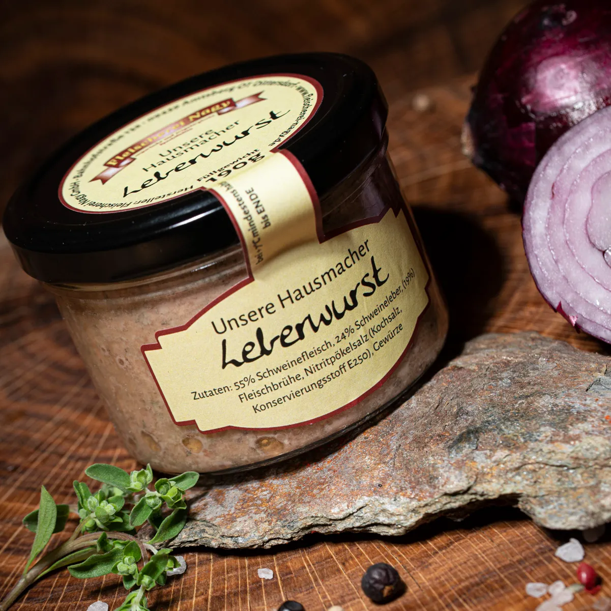 Hausmacher Leberwurst im Glas auf einem Holzbrett mit halbierter roter Zwiebel als Deko.