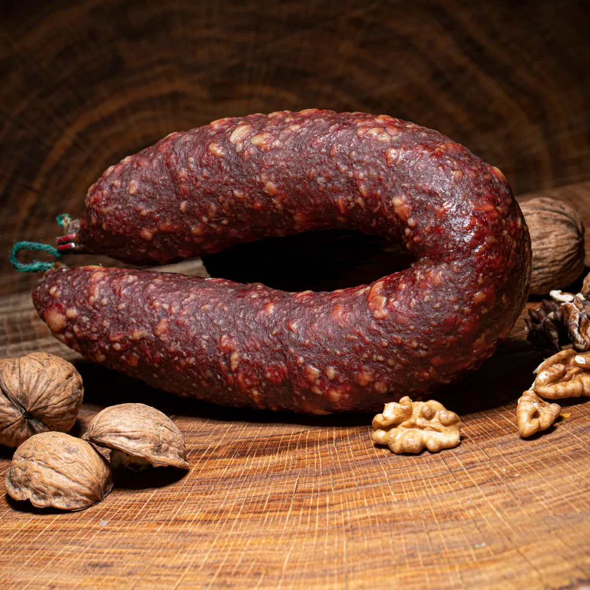 Walnusssalami gebogen auf einem Holztisch mit Walnüssen darauf als Deko.