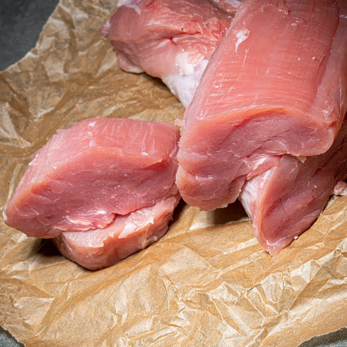 Feines Schweinefilet halbiert und an der Seite zwei kleine Scheiben Filetscheibe auf Fleischpapier.