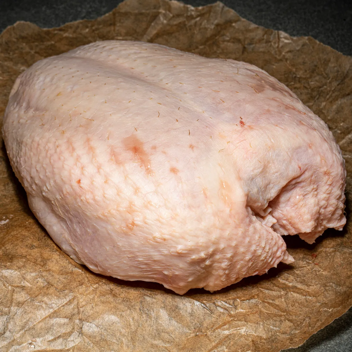Hähnchenbrustfilet mit Haut und Knochen auf Fleischpapier.