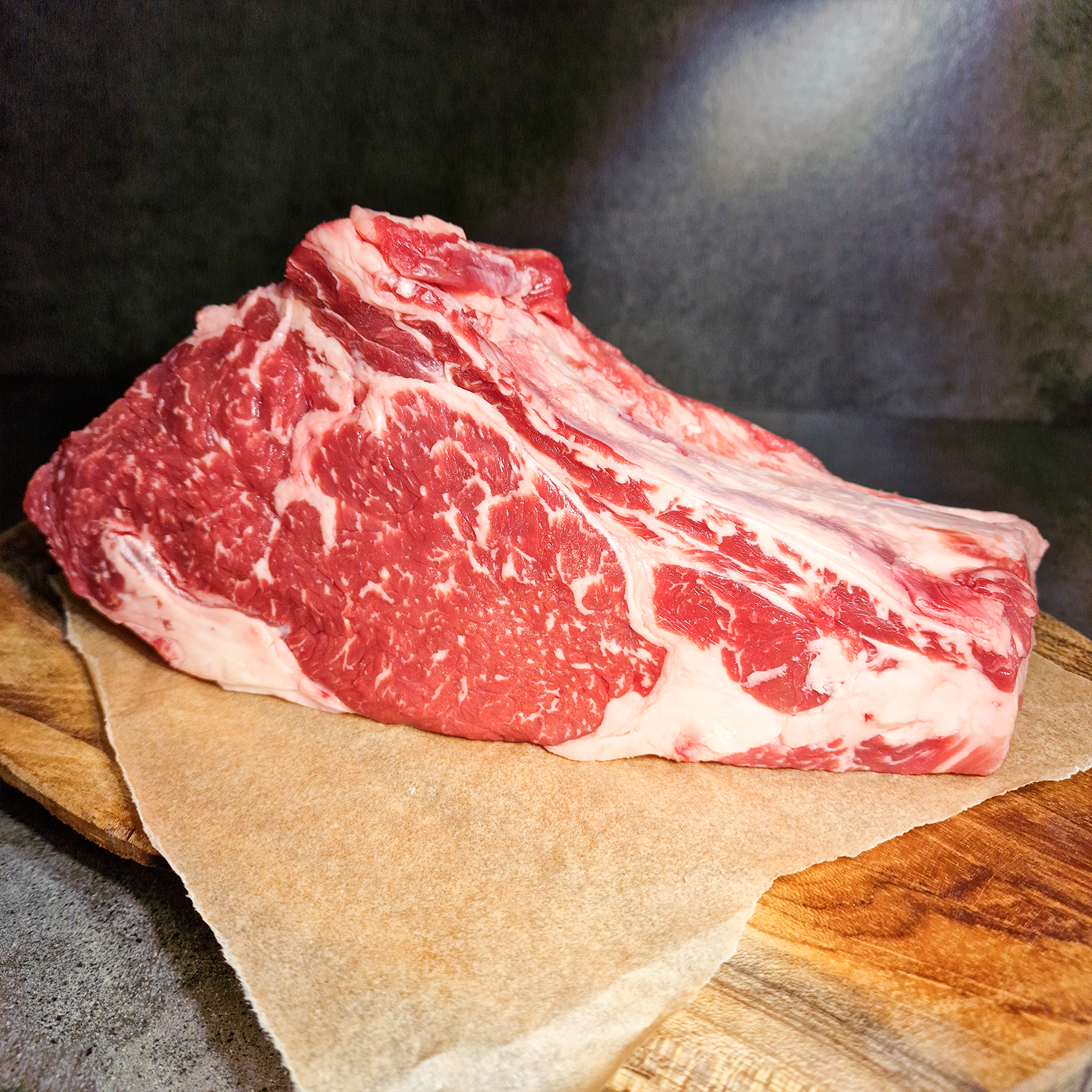 Cowboy Steak vom Angus Rind mit Knochen auf einem Holzbrett mit Fleischpapier drauf.