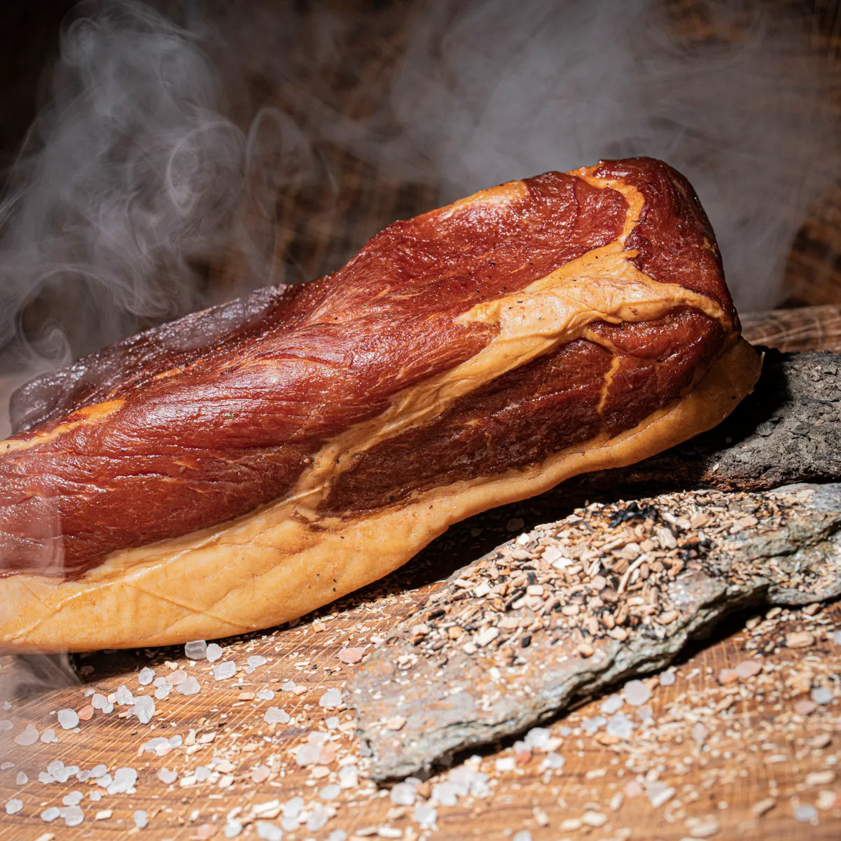 Geräucherten Mangalitza Wollschwein Schinken jetzt probieren. Mangalitza Wollschwein Schinken mit Rauch im Hintergrund mit Holzspähnen Deko.
