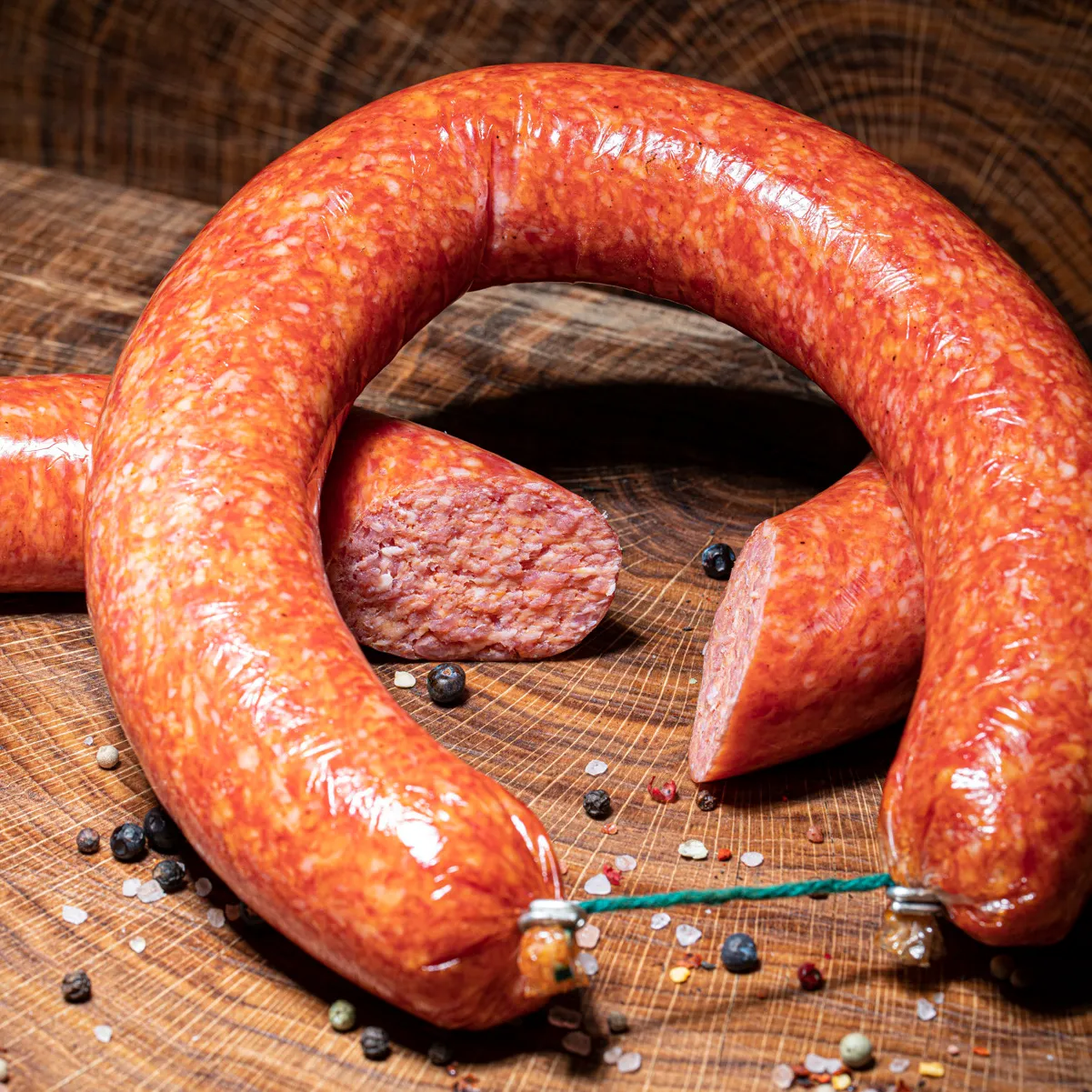 Unsere leckere grobe Mettwurst jetzt bestellen! Grobe Mettwurst ganzer Ring aufgeschnitten auf Holztisch.