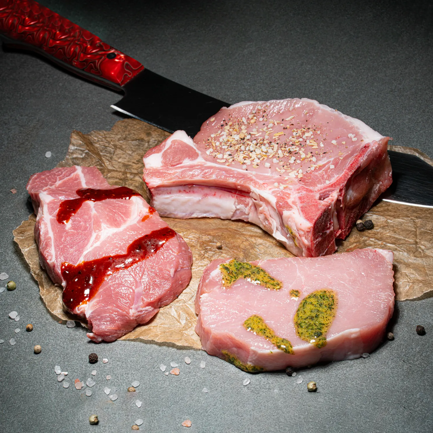 Schweinerückensteak, Schweinekammstewak und Schweinekotlett zum Grillen in feinster Marinade auf Fleischpapier.