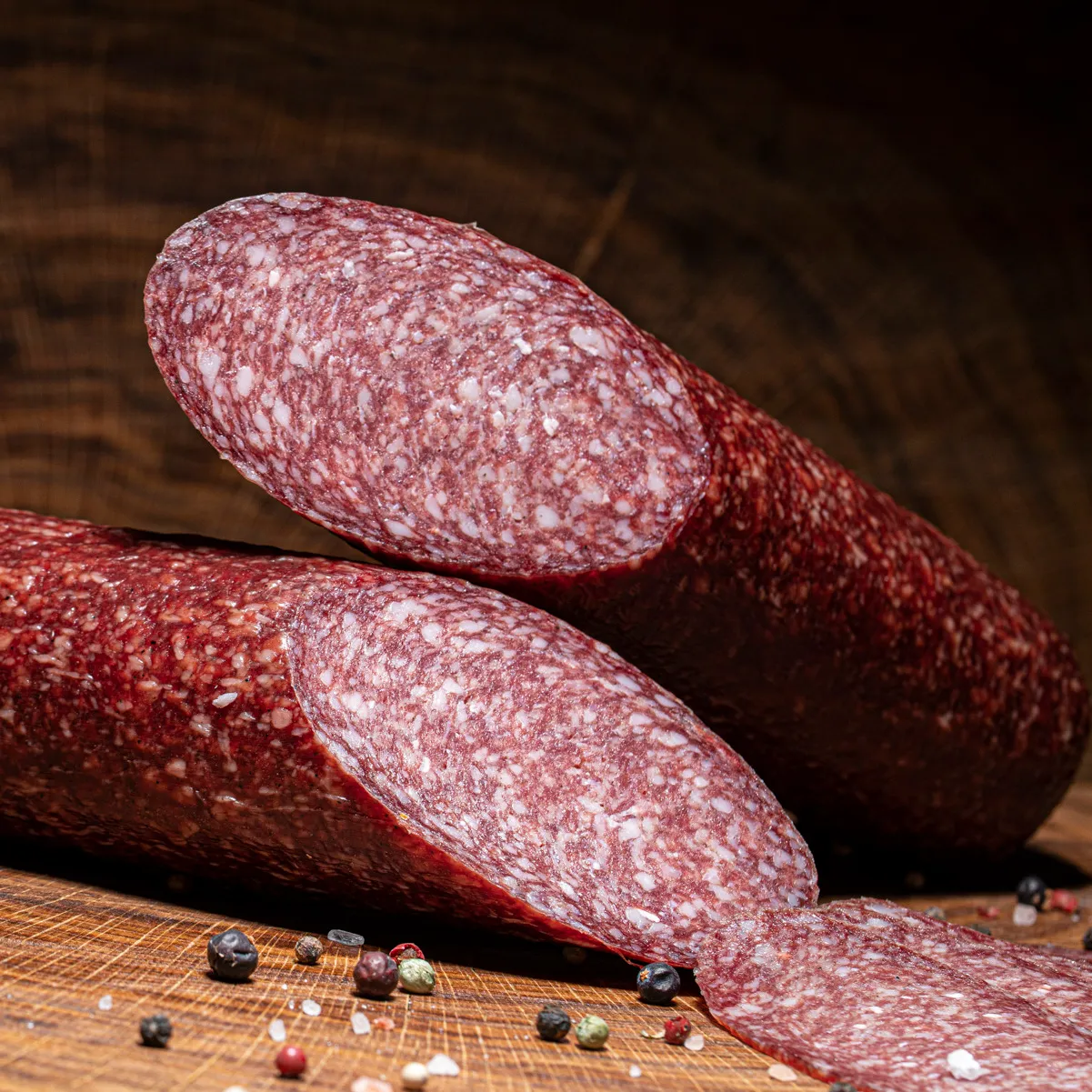 Probieren Sie unsere hauseigene Salami in groß jetzt bestellen! Hauseigene Salami groß aufgeschnitten auf einem Holztisch.