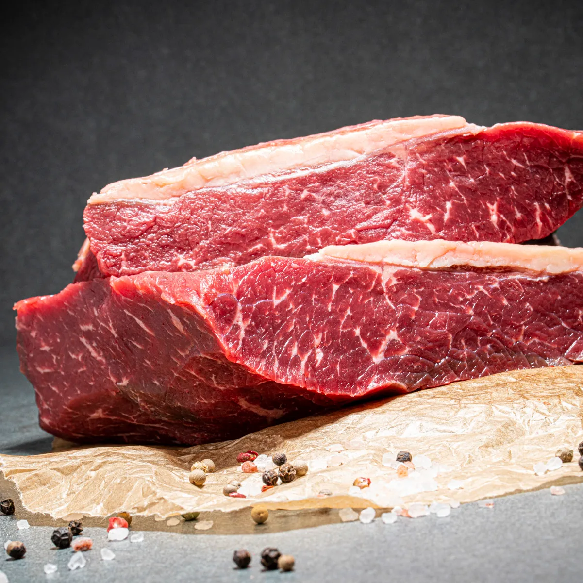 Angus Rumpsteak, zwei breite Stücke übereinander getürmt und auf Fleischpapier. Salz- und Pfefferkörnern als Deko.