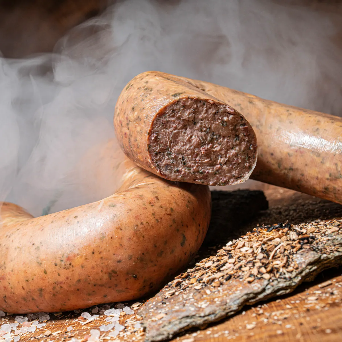 Hausmacher geräucherte Leberwurst jetzt Tradition probieren! Hausmacher geräucherte Leberwurst angeschnittener Ring mit Rauch im Hintergrund und Holzspähnen als Deko.