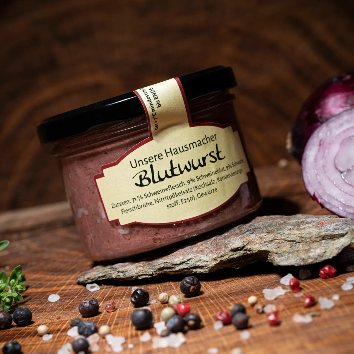 Hausmacher Blutwurst im Glas auf einem Holzbrett mit halbierter roter Zwiebel als Deko.