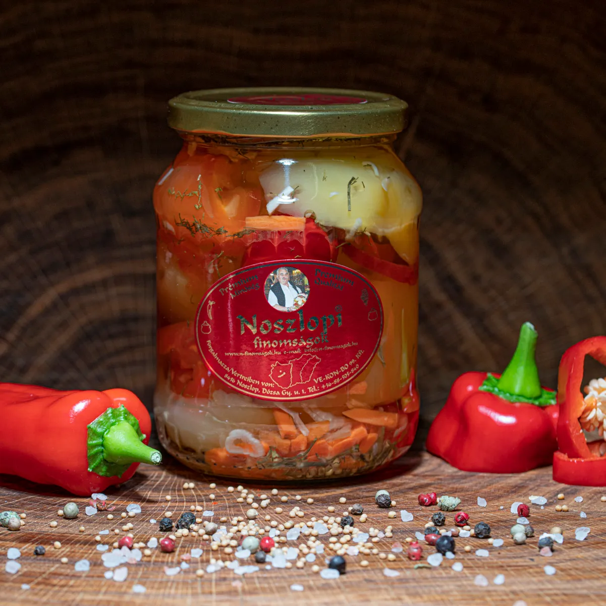 Noszlopi ungarisches Apfelpaprika in scharf im Glas jetzt probieren. Noszlopi ungarisches Apfelpaprika in scharf im Glas mit Paprika Deko auf Holzbrett.