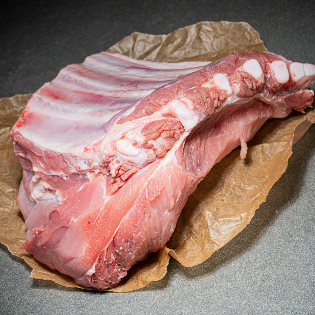 Dicke Rippe vom Schwein mit viel Fleischanteil und Knochen auf Fleischpapier.