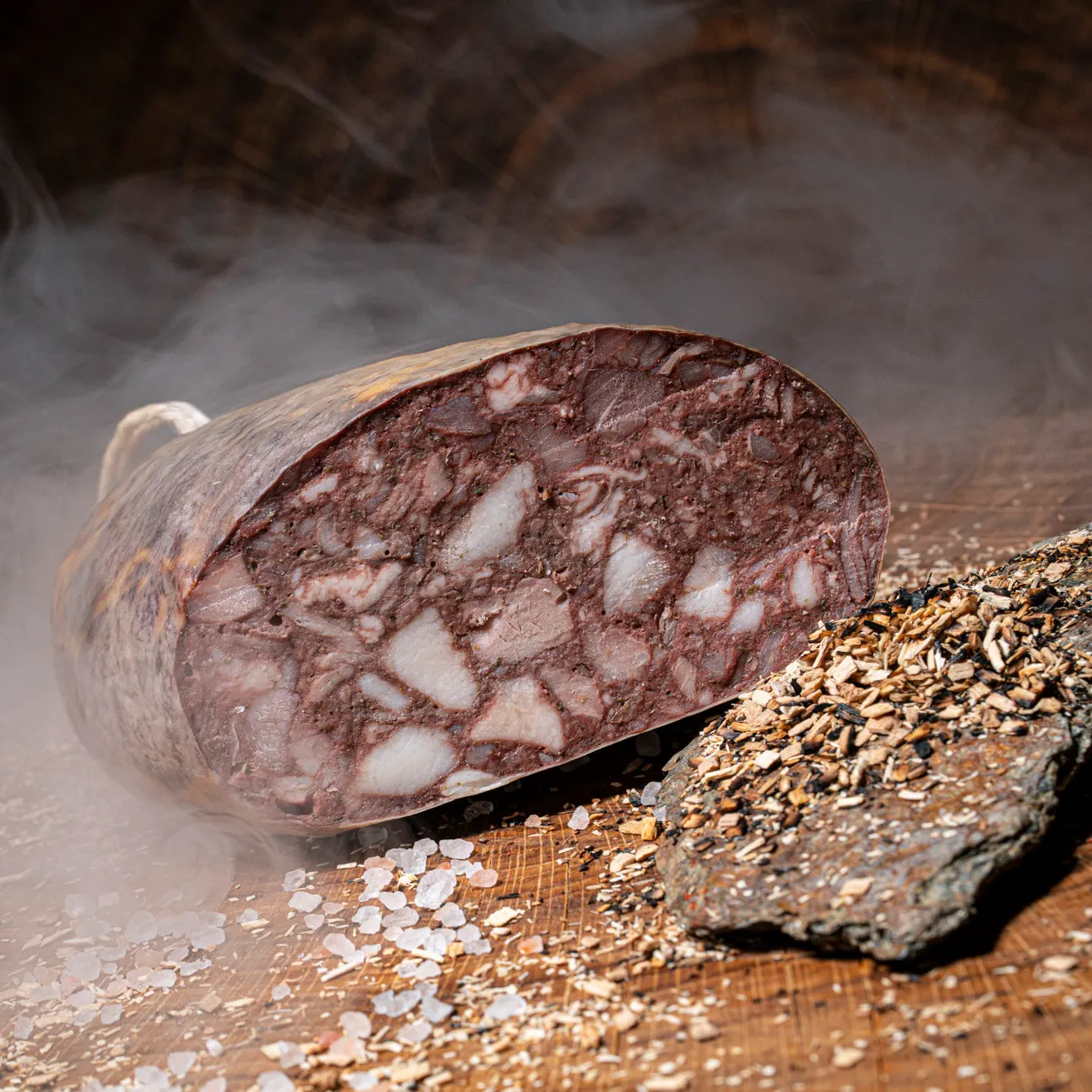 Hausmacher Blutwurst geräuchert, angeschnitten auf einem Holzbrett mit Salz- und Pfefferkörnern als Deko.