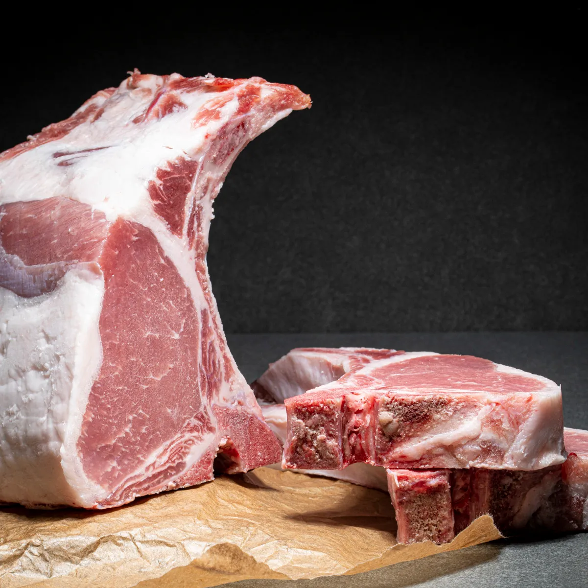 Mangalitza Kotelett am Stück, daneben liegt zwei einzelne Koteletts, alles auf Fleischpapier.