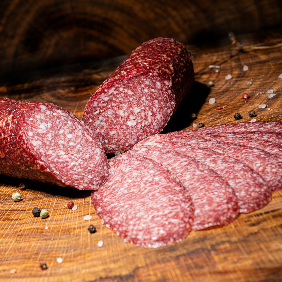 Unsere hauseigene Salami in klein jetzt kaufen! Hauseigene Salami in klein und aufgeschnitten auf einem Holztisch.