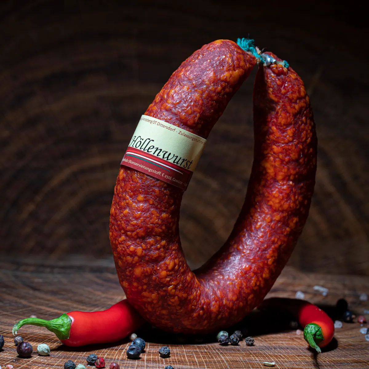 Unsere scharfe Höllenwurst als Delikatesse! Scharfe Höllenwurst mit Deko-Chili auf Tischplatte.