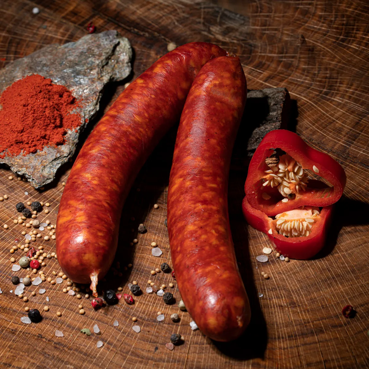 Zwei Paprikaknacker mit Salz-Pfeffer- und Paprika-Deko auf einem Holztisch.