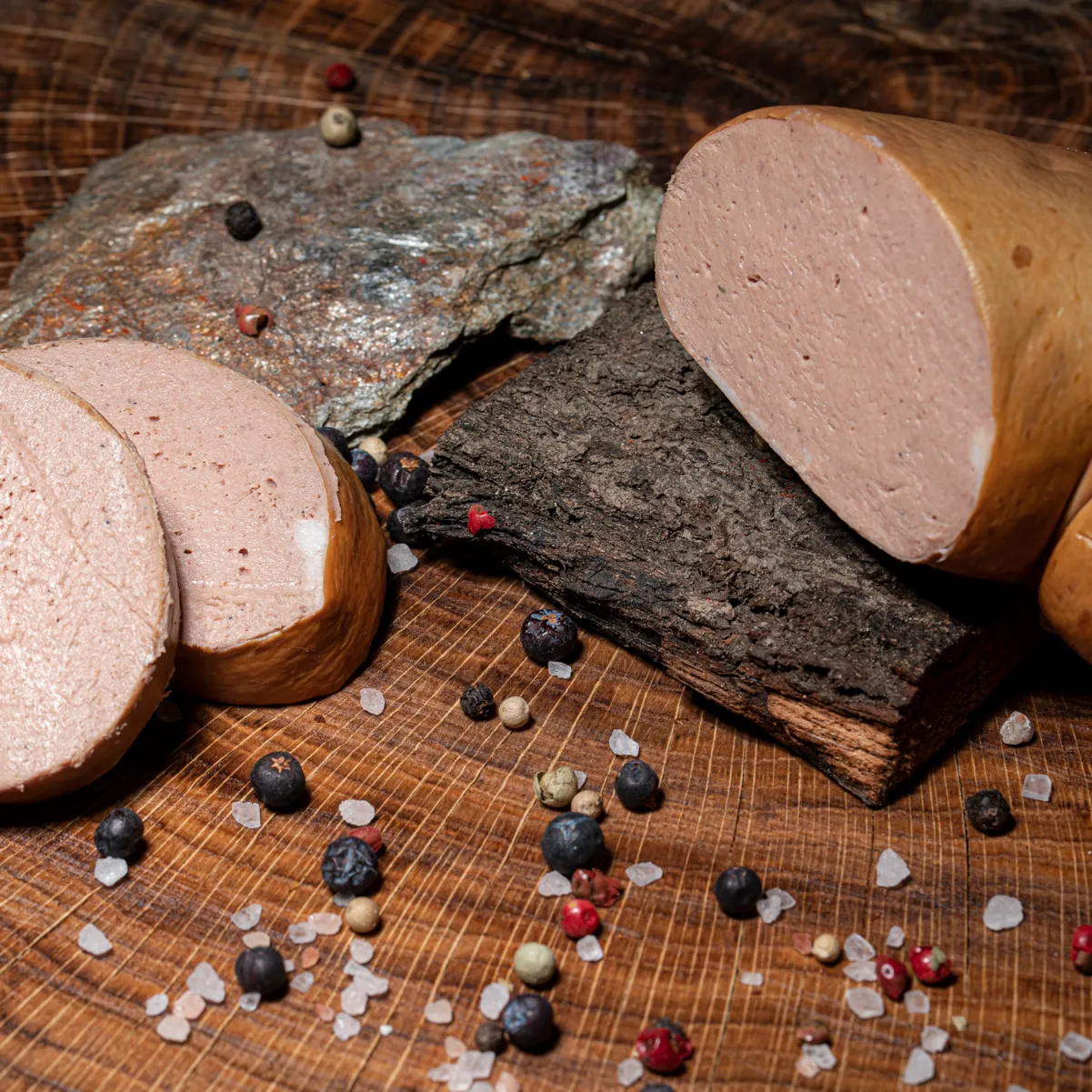 Unsere feine Leberwurst, ganz zart und lecker. Aufgeschnittene feine Leberwurst mit zwei Scheiben daneben, Pfeffer und Salz als Deko.