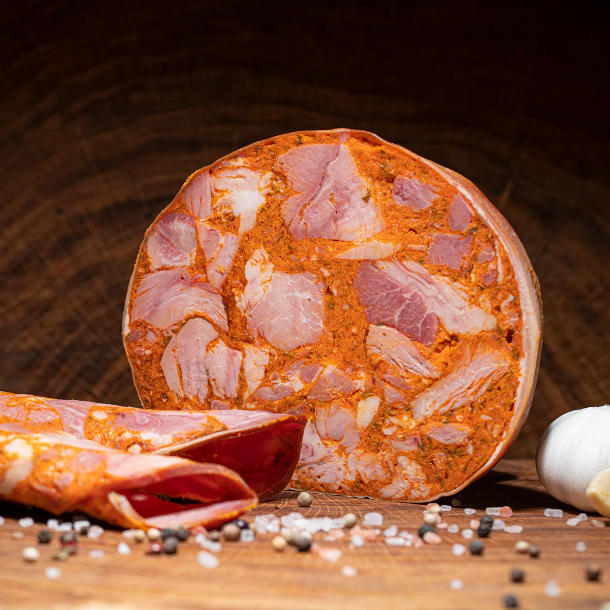 Jetzt die original ungarische Sülze bestellen! Eine Scheibe ungarische Sülze aufgeschnitten auf einer Holzplatte.