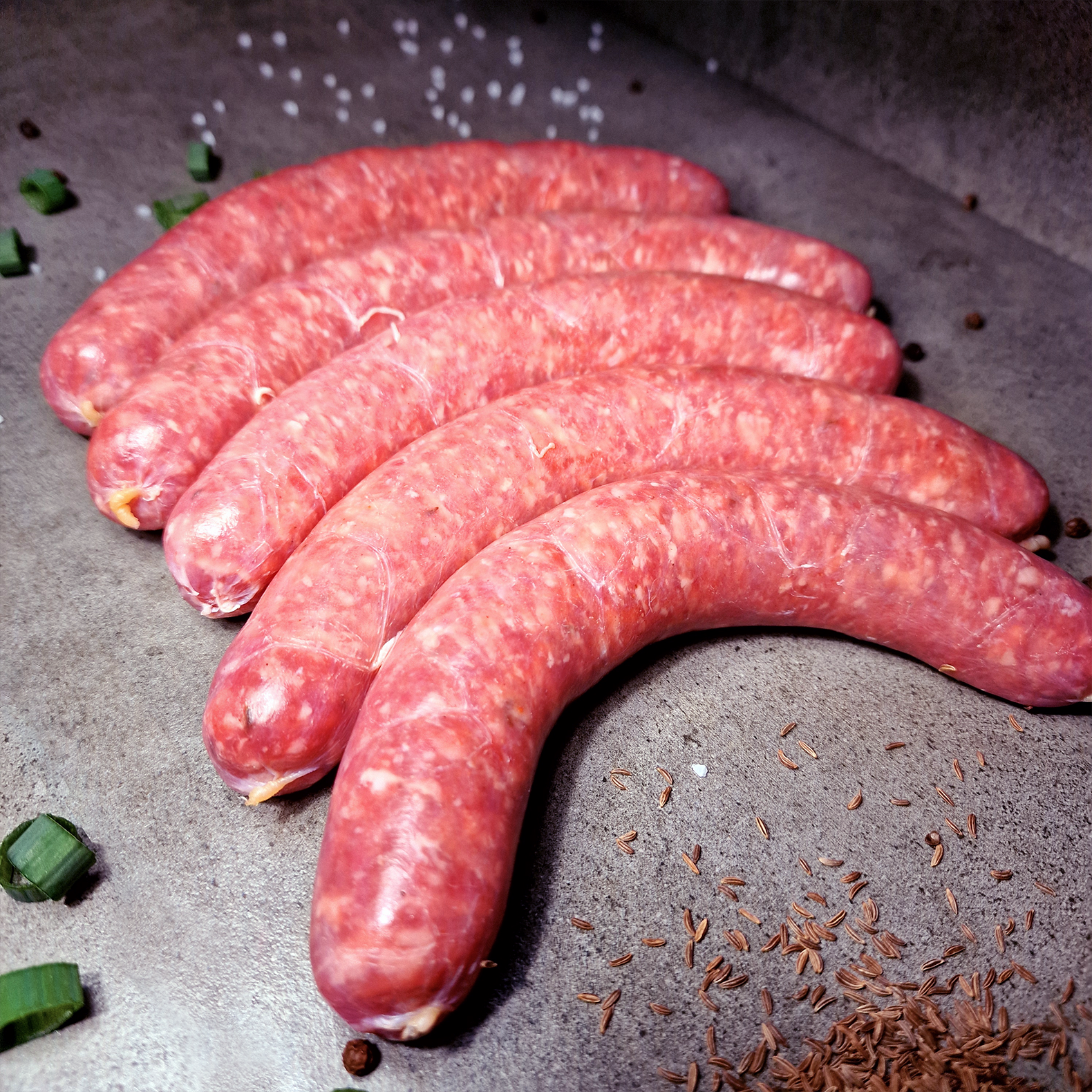 Frische grobe Bratwurst für die Pfanne oder Grill bei uns bestellen! Frische grobe Bratwurst mit Kümmel und Salz Deko auf Steinplatte.