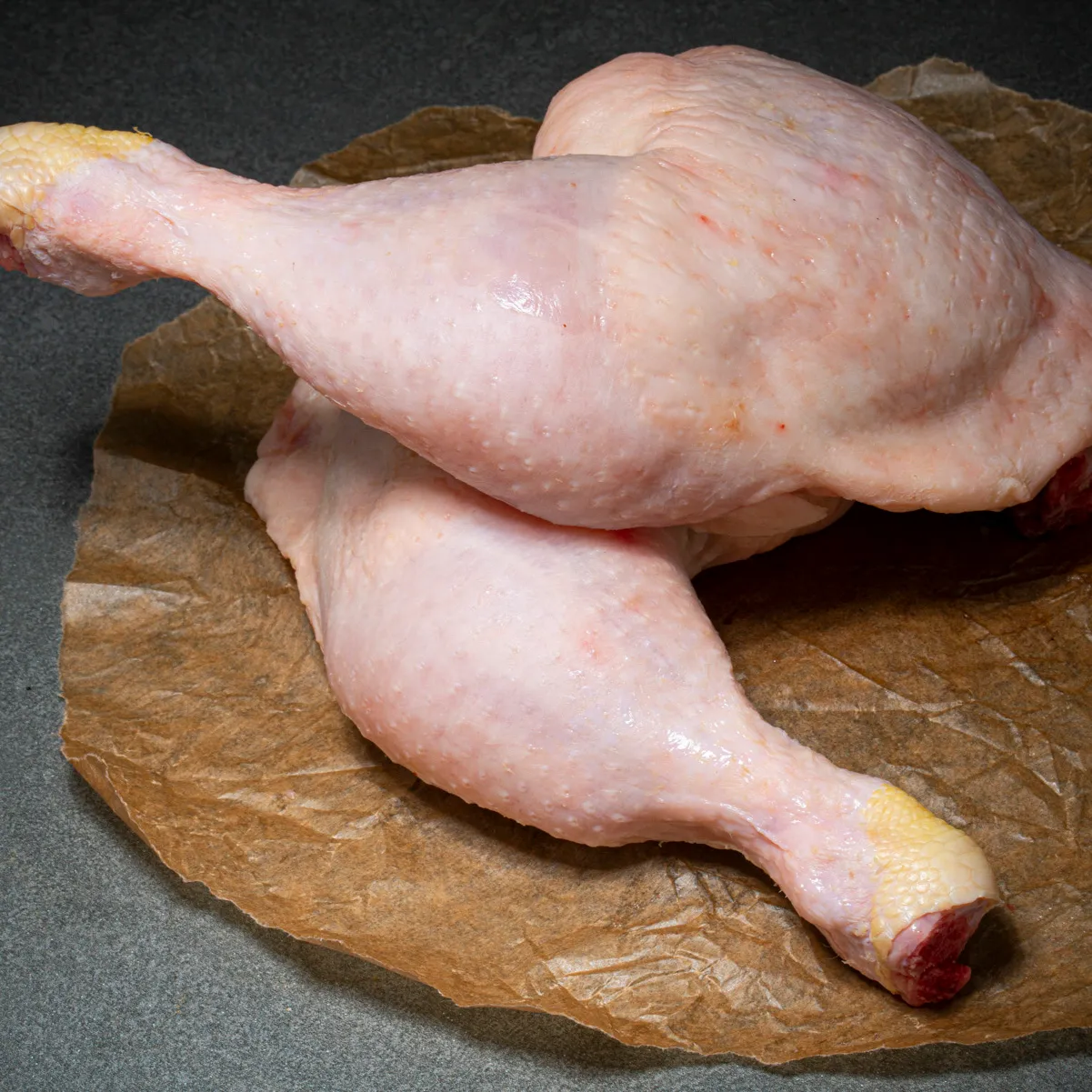 Zwei Hähnchenschenkel mit Rückenstück übereinander auf Fleischpapier.