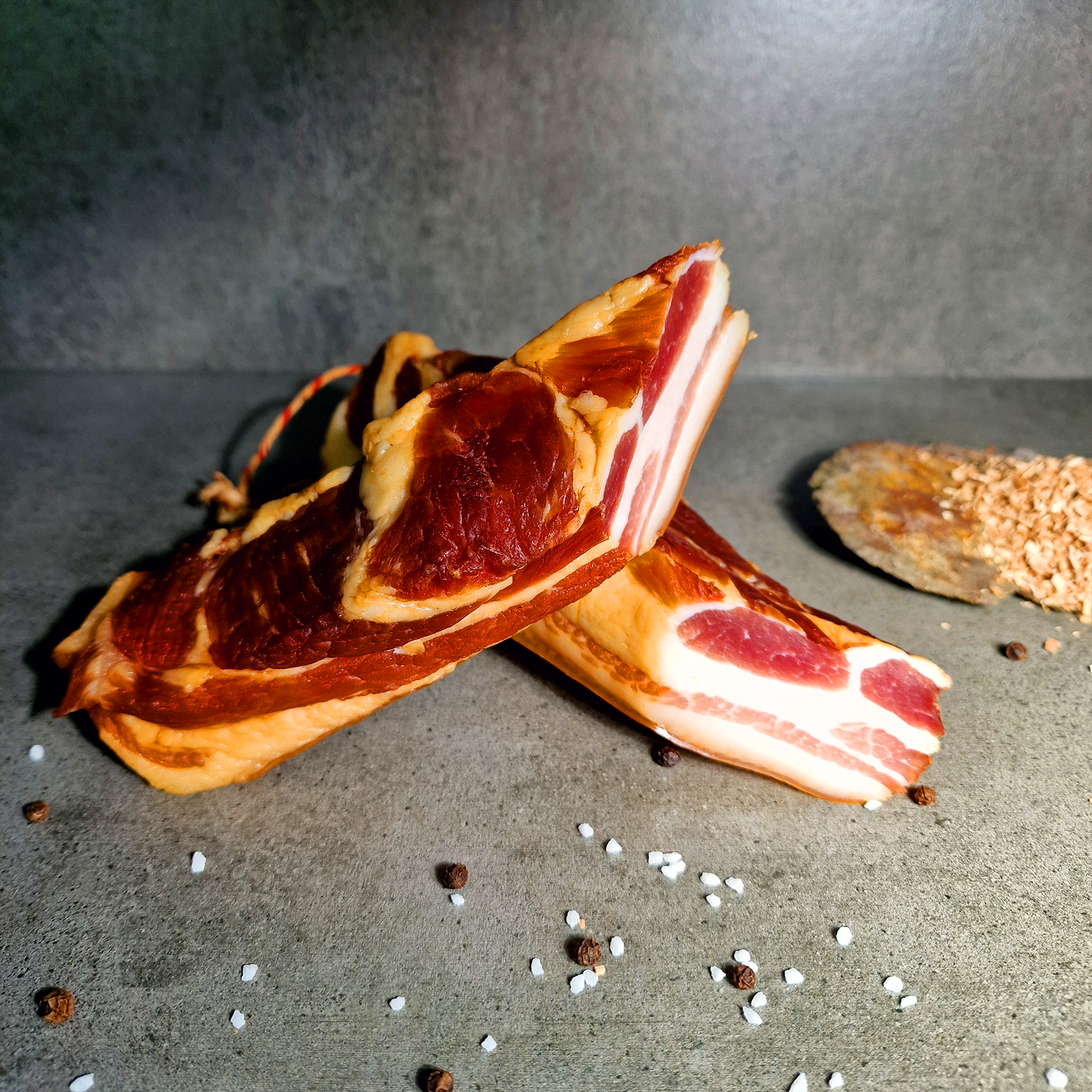 Geräucherter Kasselerbauch lecker würzig jetzt probieren! Geräucherter Kasselerbauch mit Salz-Pfeffer-Deko auf grauem Steinuntergrund.