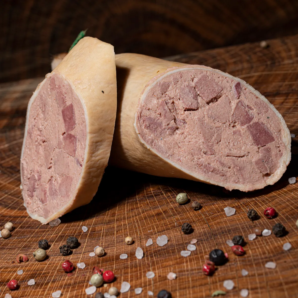 Angeschnittene Kasslerleberwurst, eine Scheibe lehnt daneben mit Salz und Pfeffer Deko auf Holzplatte.