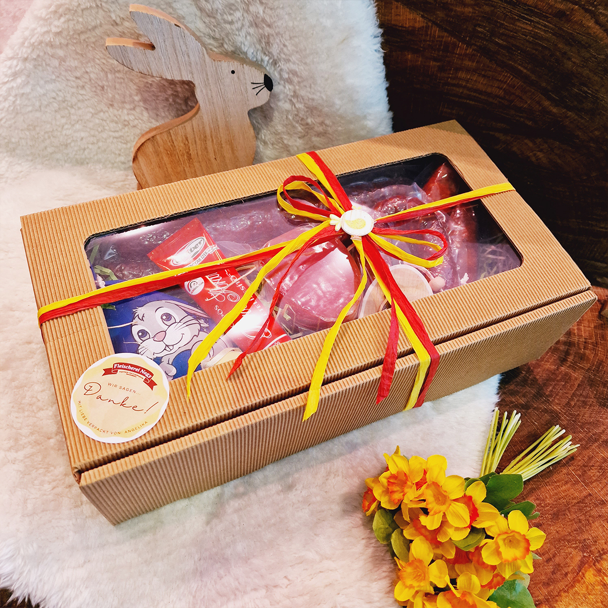 Ostergeschenkbox mit Schleife und Wurstwaren wie Rollschinken und Kümmelknacker als Inhalt.