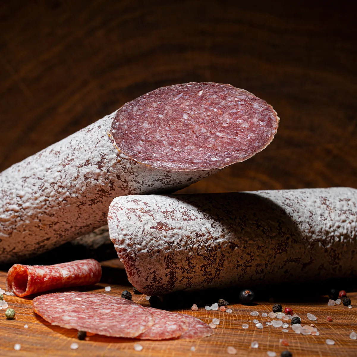 Genießen Sie unsere Mangalitzasalami als echte Besonderheit! Mangalitzasalami groß, aufgeschnitten auf Holzbrett.