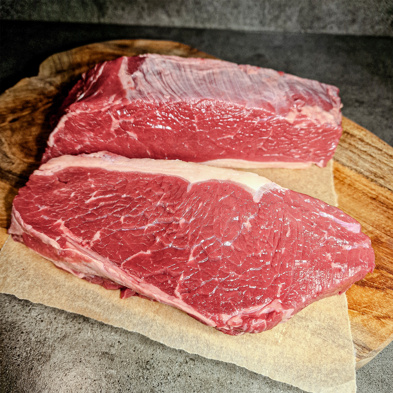 Zwei große Stücke Texas Cut vom Roastbeef geschnitten auf einem Holzbrett und Fleischpapier.