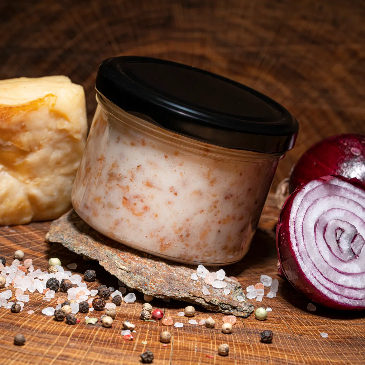 Probieren Sie unser Speckfett im Glas! Speckfett im Glas auf Holzplatte mit Zwiebel und Speck zur Deko.